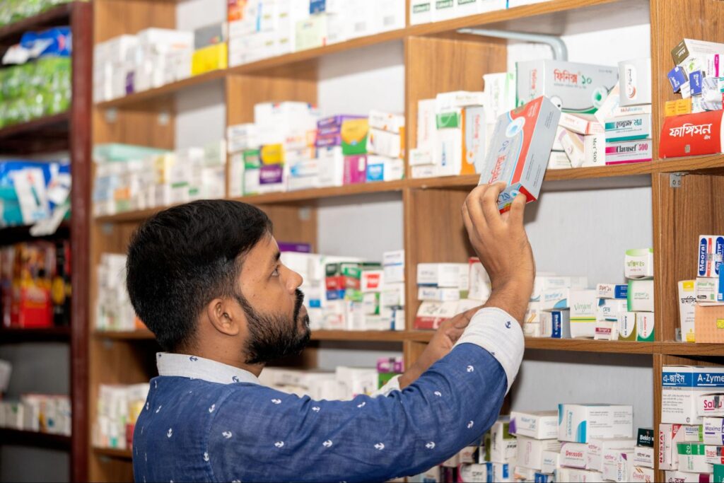A person is grabbing a rectangular medicine box from a wooden shelf, which is stocked with various medications.