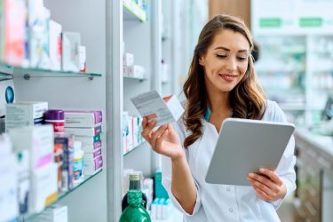 Happy female pharmacist using digital tablet while working in pharmacy.